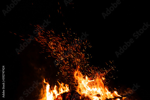 Burning red hot sparks rise from large fire in the night. Fire flames sparks background. Abstract dark glitter fire particles lights.