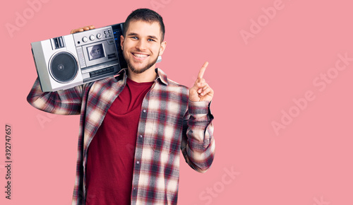 Young handsome man listening to music holding boombox surprised with an idea or question pointing finger with happy face, number one