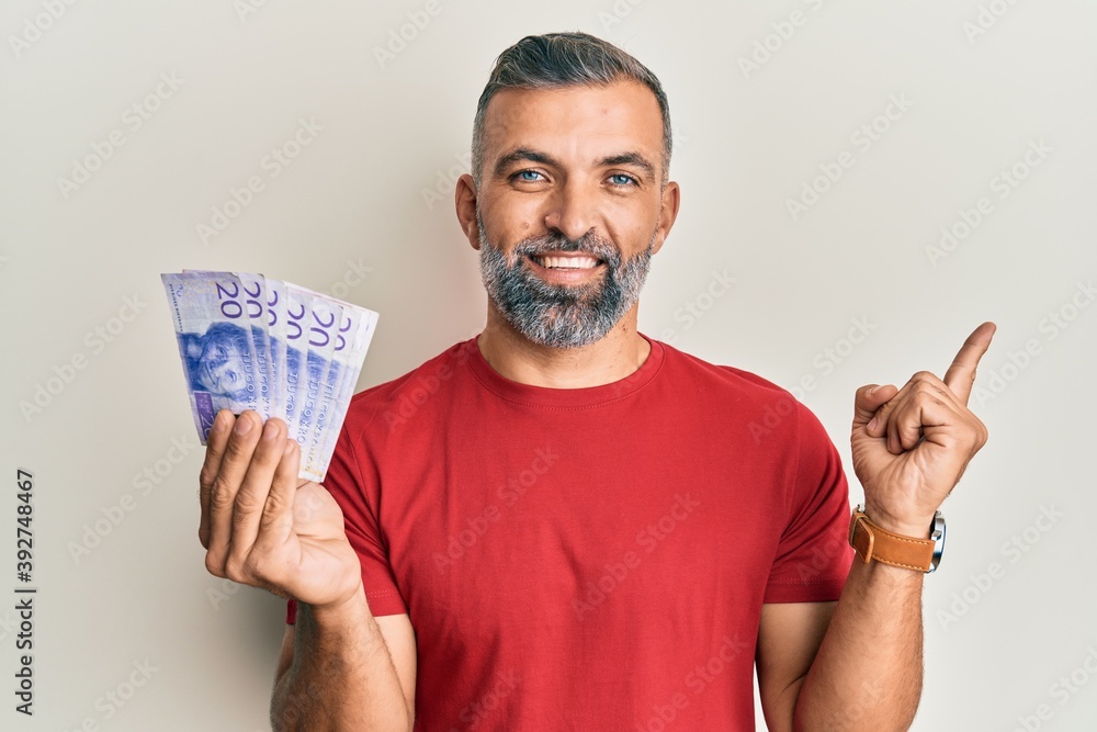 Middle age handsome man holding 20 swedish krona banknotes smiling happy pointing with hand and finger to the side Middle age handsome man holding 20 swedish krona banknotes smiling happy pointing with hand and finger to the side