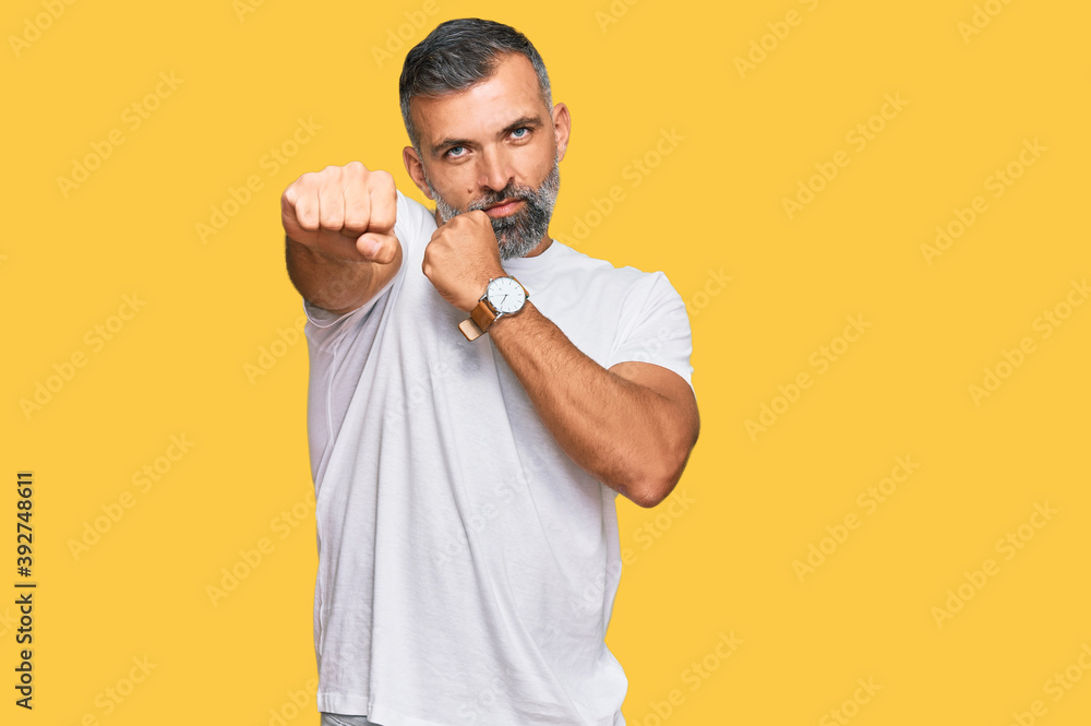 Middle age handsome man wearing casual white tshirt punching fist to fight, aggressive and angry attack, threat and violence Middle age handsome man wearing casual white tshirt punching fist to fight, aggressive and angry attack, threat and violence