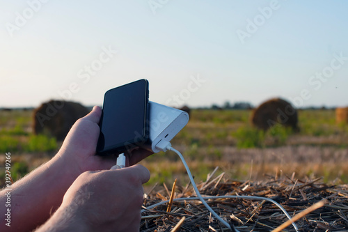 A man holds a smartphone and a portable charger in his hands against the backdrop of nature and the sky. Power Bank charges your phone while traveling.