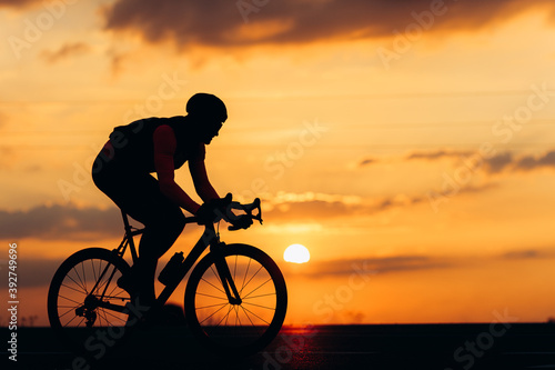 Sporty man in silhouette riding bike on paved road