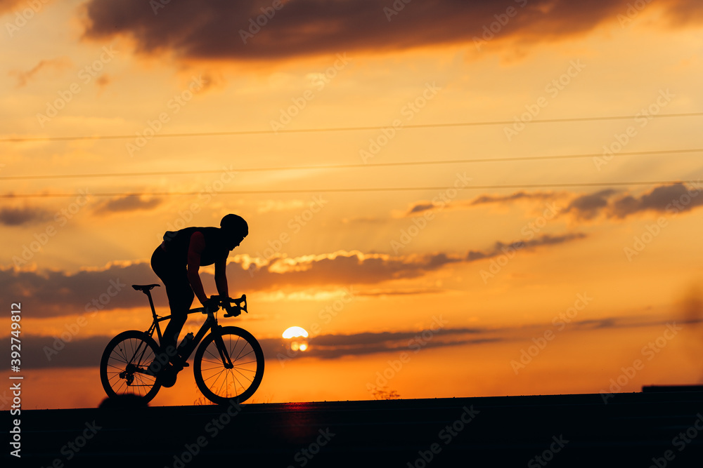 Obraz premium Muscular man biking on road during amazing sunset