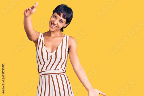 Young brunette woman with short hair wearing summer outfit looking at the camera smiling with open arms for hug. cheerful expression embracing happiness.