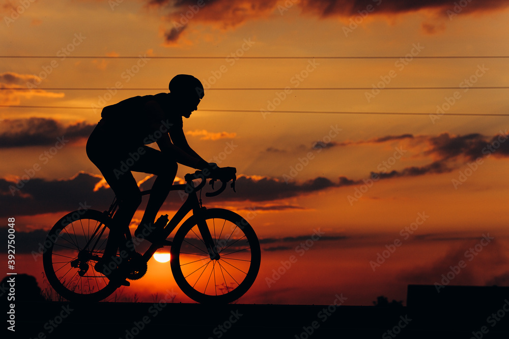Obraz premium Athletic cyclist in silhouette racing on road