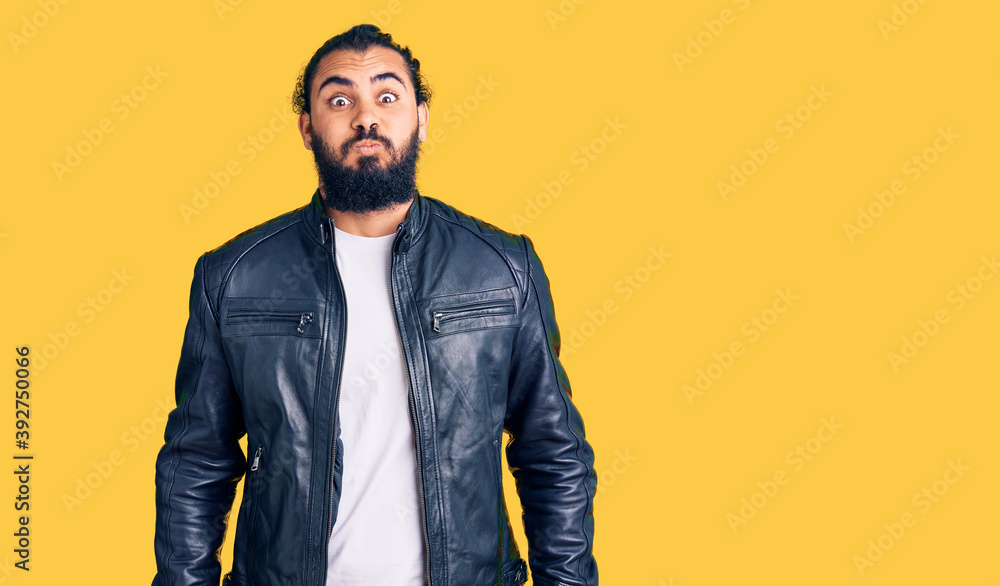 Fototapeta premium Young arab man wearing casual leather jacket puffing cheeks with funny face. mouth inflated with air, crazy expression.