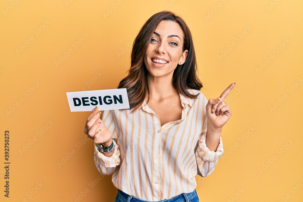 Young brunette woman holding design paper smiling happy pointing with hand and finger to the side Young brunette woman holding design paper smiling happy pointing with hand and finger to the side