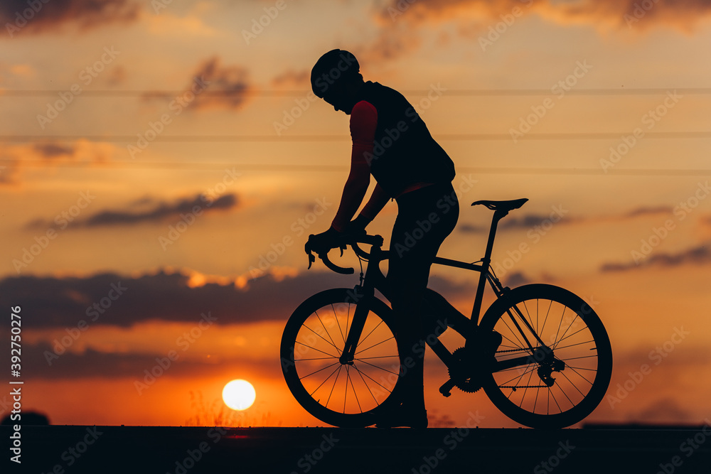 Fototapeta premium Athletic man in silhouette posing on camera with bike
