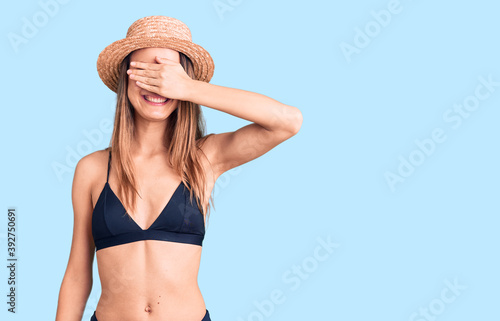 Young beautiful girl wearing bikini and hat smiling and laughing with hand on face covering eyes for surprise. blind concept.