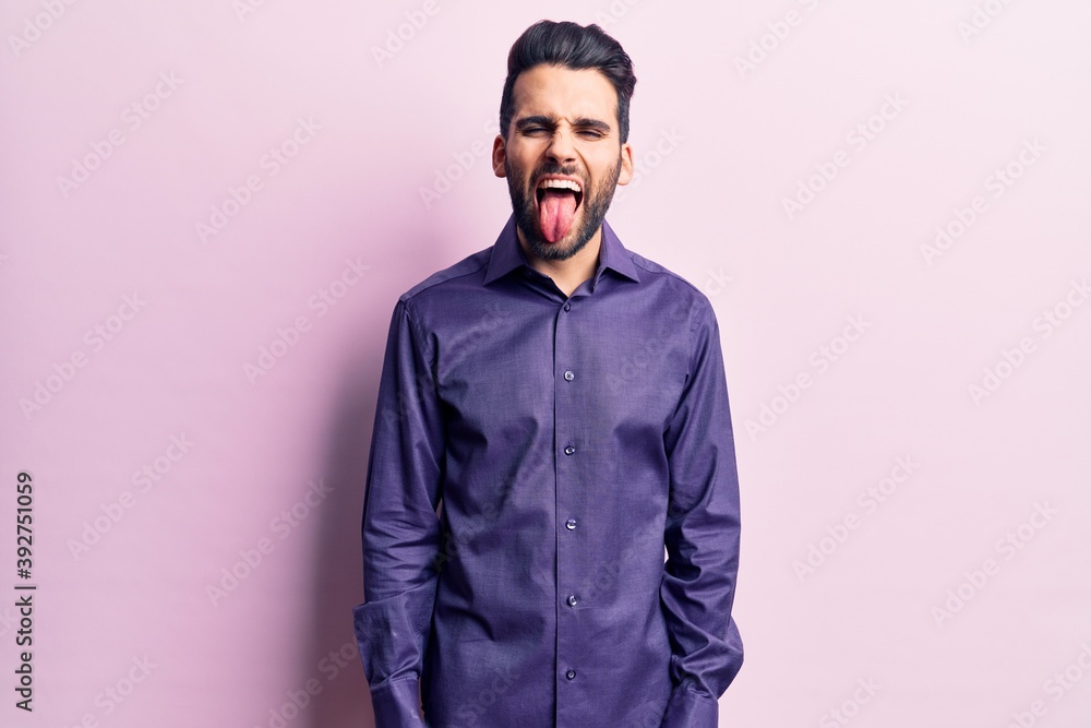 Fototapeta premium Young handsome man with beard wearing casual shirt sticking tongue out happy with funny expression. emotion concept.