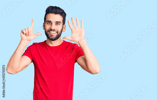 Young handsome man with beard wearing casual t-shirt showing and pointing up with fingers number seven while smiling confident and happy.