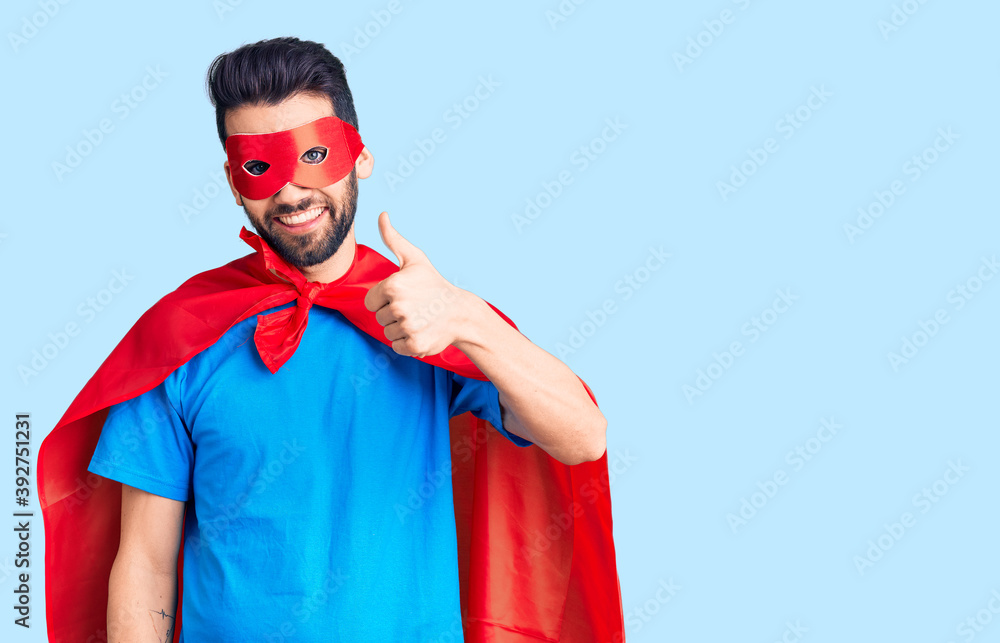 Young handsome man with beard wearing super hero costume doing happy thumbs up gesture with hand. approving expression looking at the camera showing success. Young handsome man with beard wearing super hero costume doing happy thumbs up gesture with hand. approving expression looking at the camera showing success.