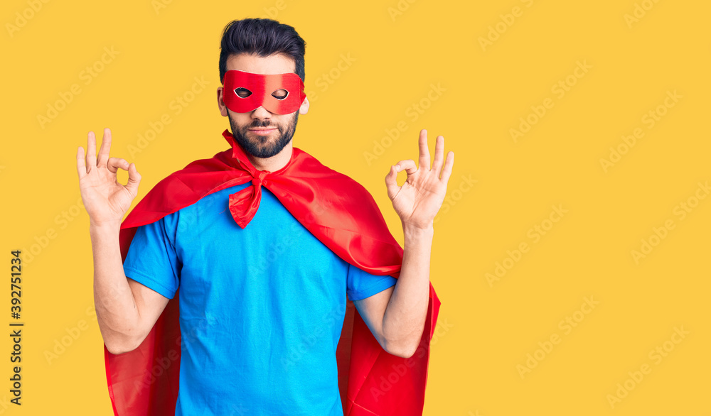Young handsome man with beard wearing super hero costume relax and smiling with eyes closed doing meditation gesture with fingers. yoga concept. Young handsome man with beard wearing super hero costume relax and smiling with eyes closed doing meditation gesture with fingers. yoga concept.