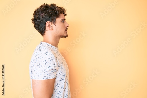 Young caucasian man with curly hair wearing casual clothes looking to side, relax profile pose with natural face with confident smile.