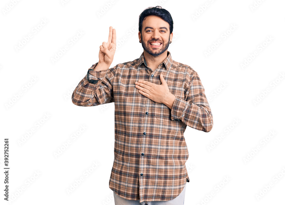 Naklejka premium Young hispanic man wearing casual clothes smiling swearing with hand on chest and fingers up, making a loyalty promise oath