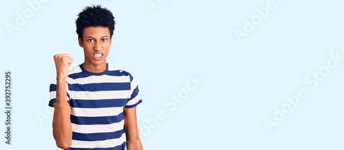 Young african american man wearing casual clothes angry and mad raising fist frustrated and furious while shouting with anger. rage and aggressive concept.