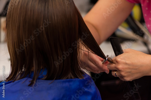 Professional female hairdresser cutting girl's hair in salon