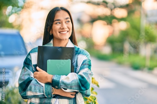 Obraz na plátně Young latin student girl smiling happy holding folder at the city