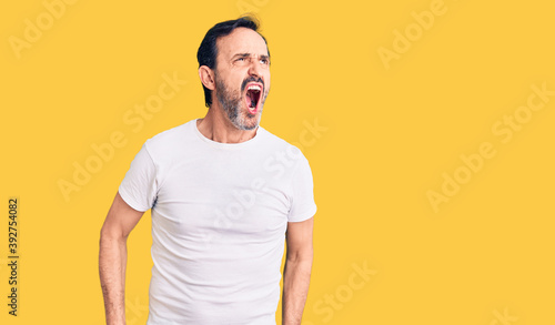 Middle age handsome man wearing casual t-shirt angry and mad screaming frustrated and furious, shouting with anger. rage and aggressive concept.