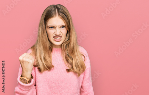 Beautiful young caucasian girl wearing casual winter sweater angry and mad raising fist frustrated and furious while shouting with anger. rage and aggressive concept.
