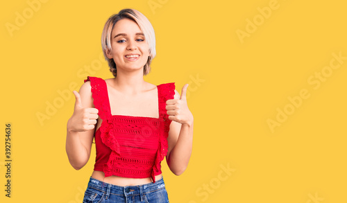 Young beautiful blonde woman wearing casual clothes success sign doing positive gesture with hand  thumbs up smiling and happy. cheerful expression and winner gesture.