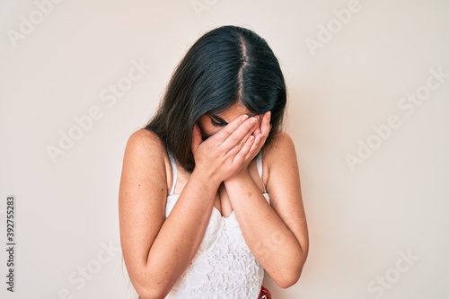 Brunette teenager girl posing elegant with sad expression covering face with hands while crying. depression concept.