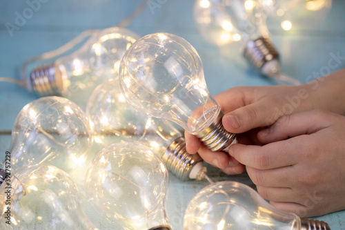 children's hand with a decorative light bulb garland on a light wooden surface
