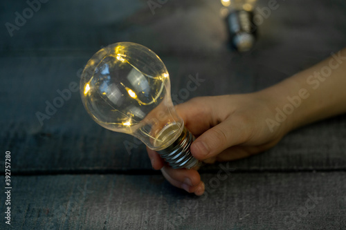 children's hand with a decorative light bulb garland on a light wooden surface