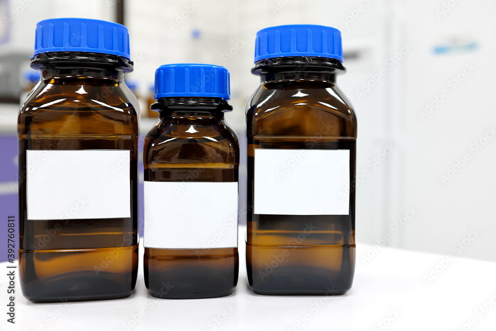 Selective focus of three dark glass reagent bottle with unknown clear liquid chemical inside and blank label in a chemistry laboratory. Selective focus of three dark glass reagent bottle with unknown clear liquid chemical inside and blank label in a chemistry laboratory.