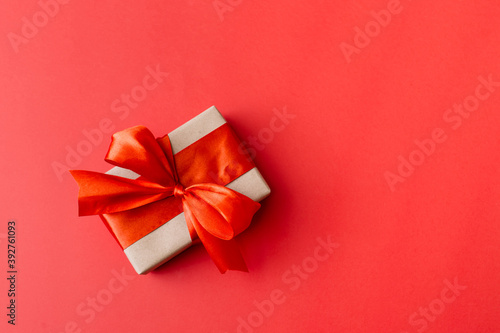 Present box with red bow on red background. Flat lay, top view, copy space.