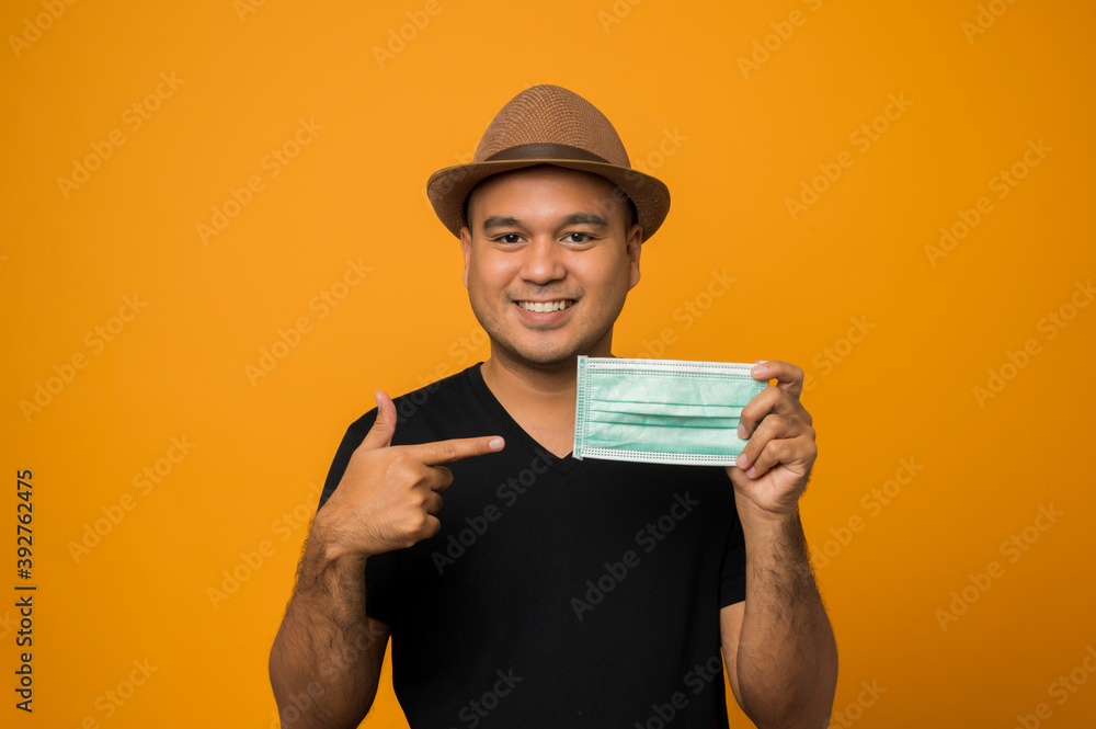 Guy in hat wearing casual clothes pointing finger to face mask isolated on yellow background Guy in hat wearing casual clothes pointing finger to face mask isolated on yellow background
