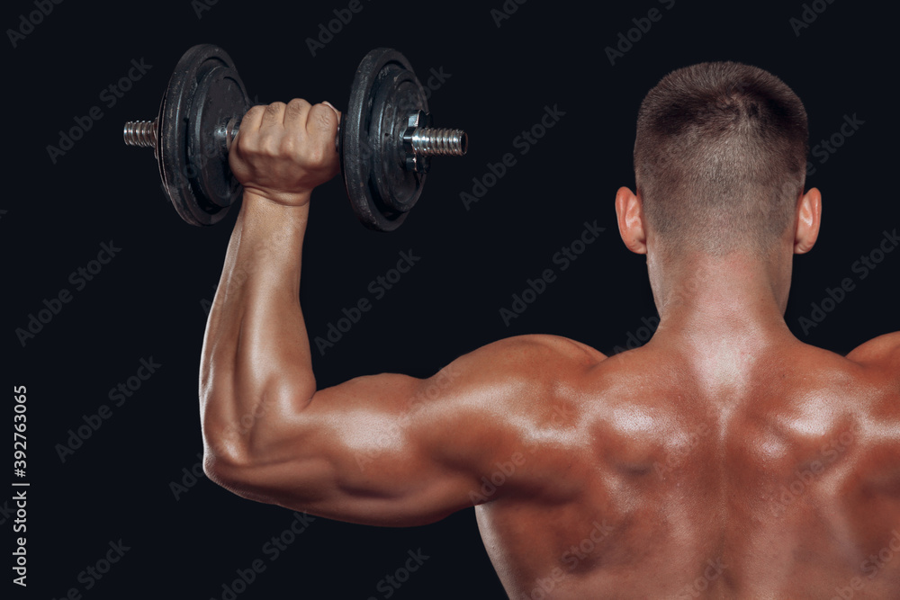 Close up back view on bodybuilders strong muscular arm lifting a dumbbell isolated on black background