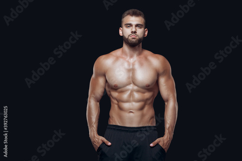 Muscular and fit young bodybuilder fitness male model posing isolated on black background