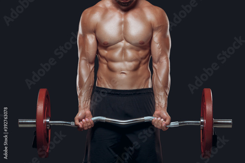 Close up of strong bodybuilder muscular arms lifting a barbell isolated on black background