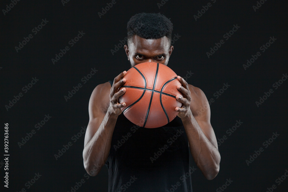 Close up front view shot of afro american male basketball player holding a ball in front of him over black background