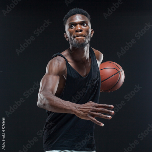 Portrait of afro american male basketball player playing with a ball over black background. Fit young man in sportswear holding basketball © satyrenko