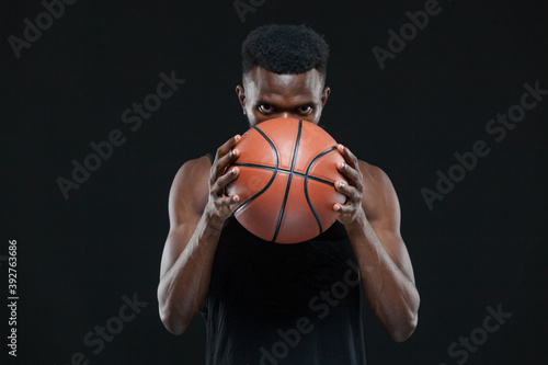 Close up front view shot of afro american male basketball player holding a ball in front of him over black background