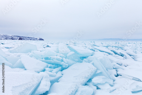Frosen Lake Baikal on a cold February day. Boundless ice fields of snow-covered hummocks of pieses of blue ice near the snowy Olkhon Island. Winter travel. Natural background