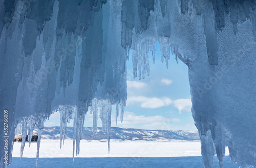 Cold winter landscape with long icicles in an icy grotto. Natural blue background for seasonal calendar. Baikal Lake. View on the Small Sea Strait from rocky shore of Olkhon Island. Winter holidays