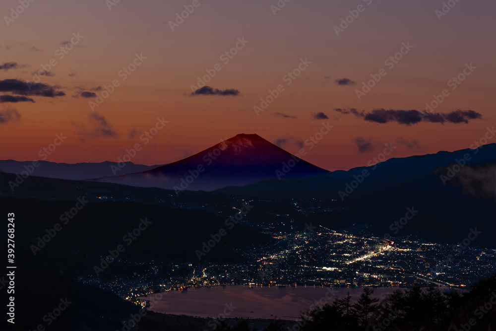 富士山を赤く染める日の出前の薄明かりと、諏訪湖麺の販社と諏訪市の街灯り