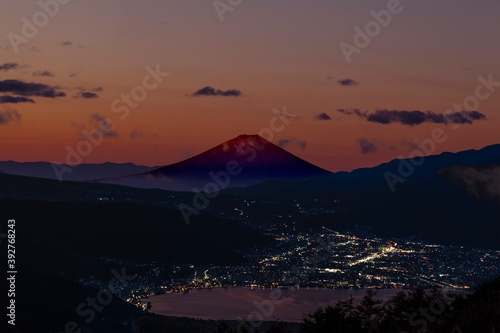 富士山を赤く染める日の出前の薄明かりと、諏訪湖麺の販社と諏訪市の街灯り