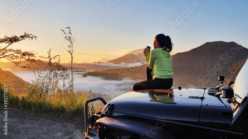 Woman sit on car hood while enjoy mount batur view photo
