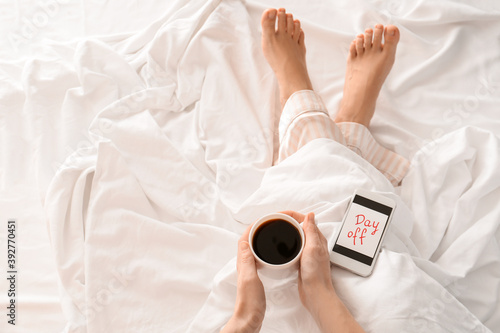 Woman with cup of coffee relaxing in bed. Concept of day off