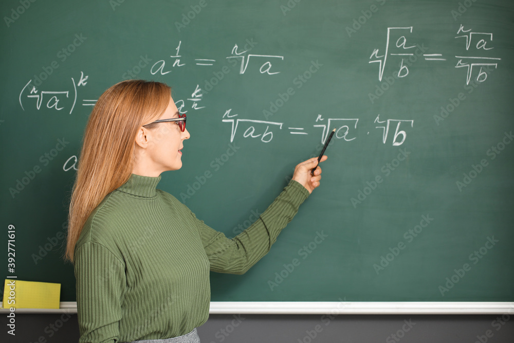 Mature maths teacher near blackboard in classroom