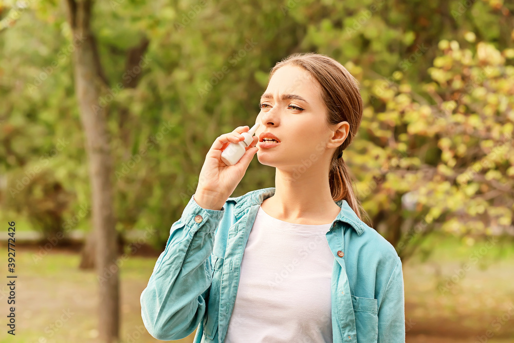 Allergic young woman using nasal drops outdoors