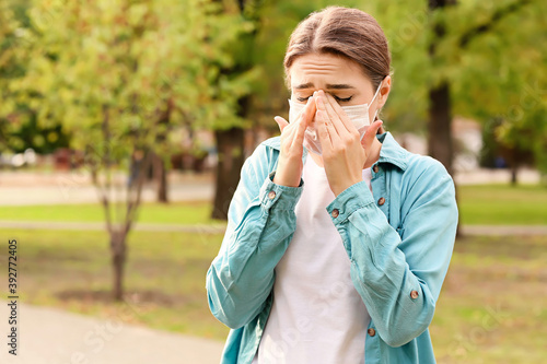 Young woman in medical mask suffering from allergy outdoors