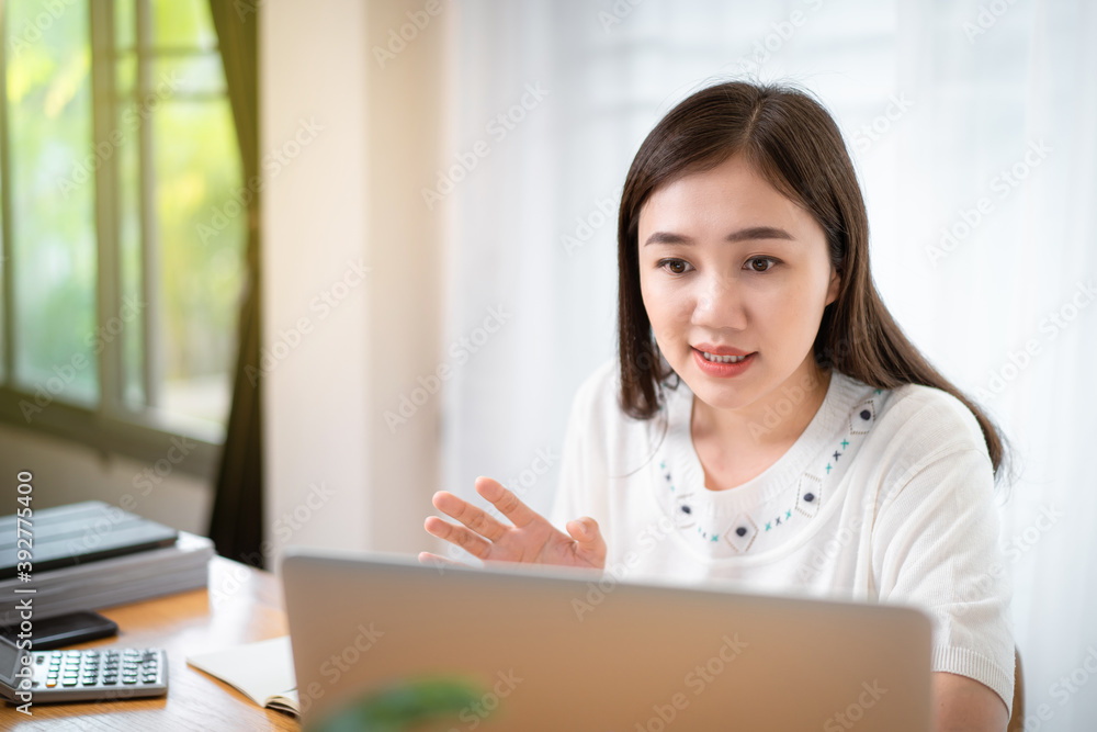 Happy Asian young woman working at home, working from home is the new working solution during the COVID-19 pandemic and able to increase working productivity. Asian beautiful girl using video call. Happy Asian young woman working at home, working from home is the new working solution during the COVID-19 pandemic and able to increase working productivity. Asian beautiful girl using video call.