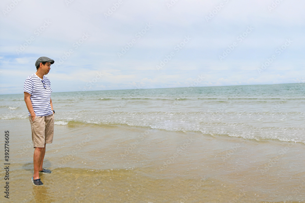 A man is standing on the beach looking at the sea. Wide angle shot.