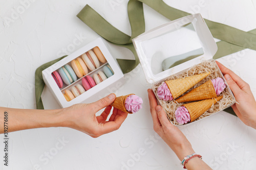 Female hand passing sweet zefir cone to the woman holding box full of them photo