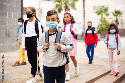 Focused hispanic tweenager in medical face mask with backpack going to school lessons on warm autumn day. New lifestyle during coronavirus pandemic.